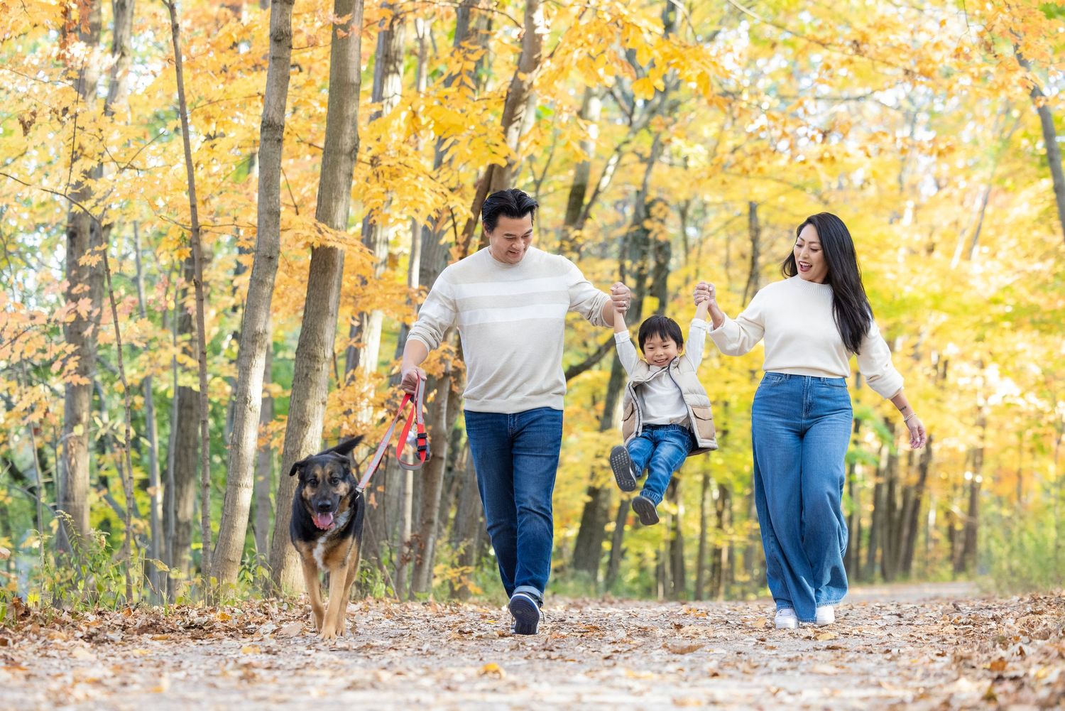 A family walks together through a vibrant autumn forest with golden yellow leaves during a fall photoshoot session.