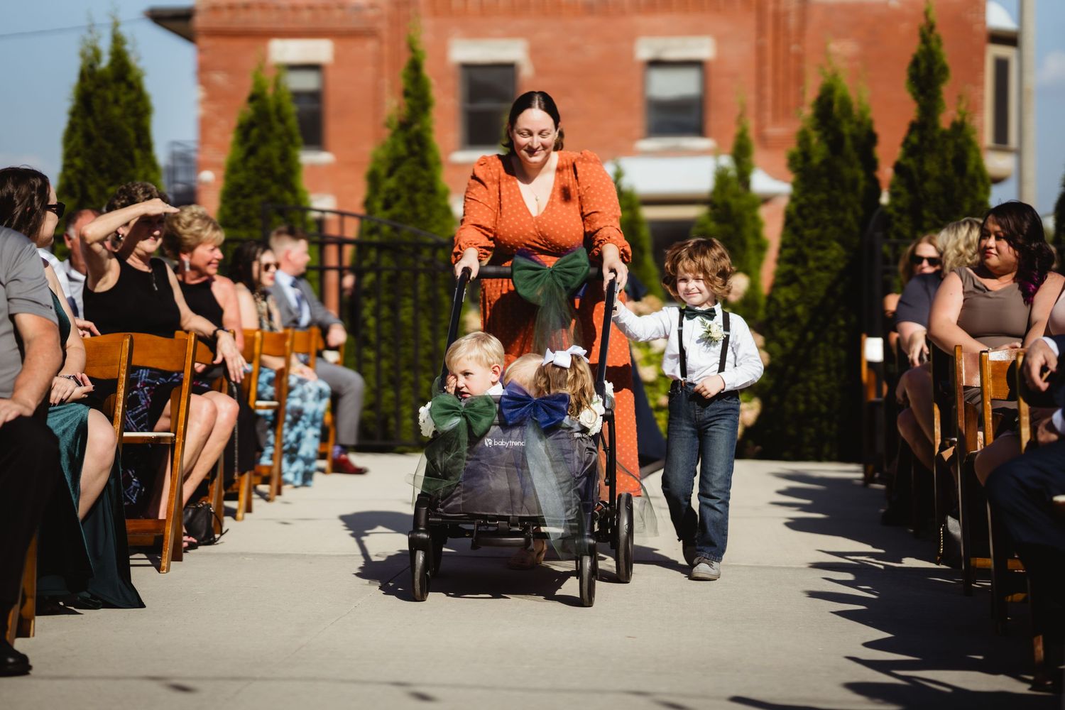 Joyful outdoor wedding procession on a sunny day with guests seated along both sides of the aisle.