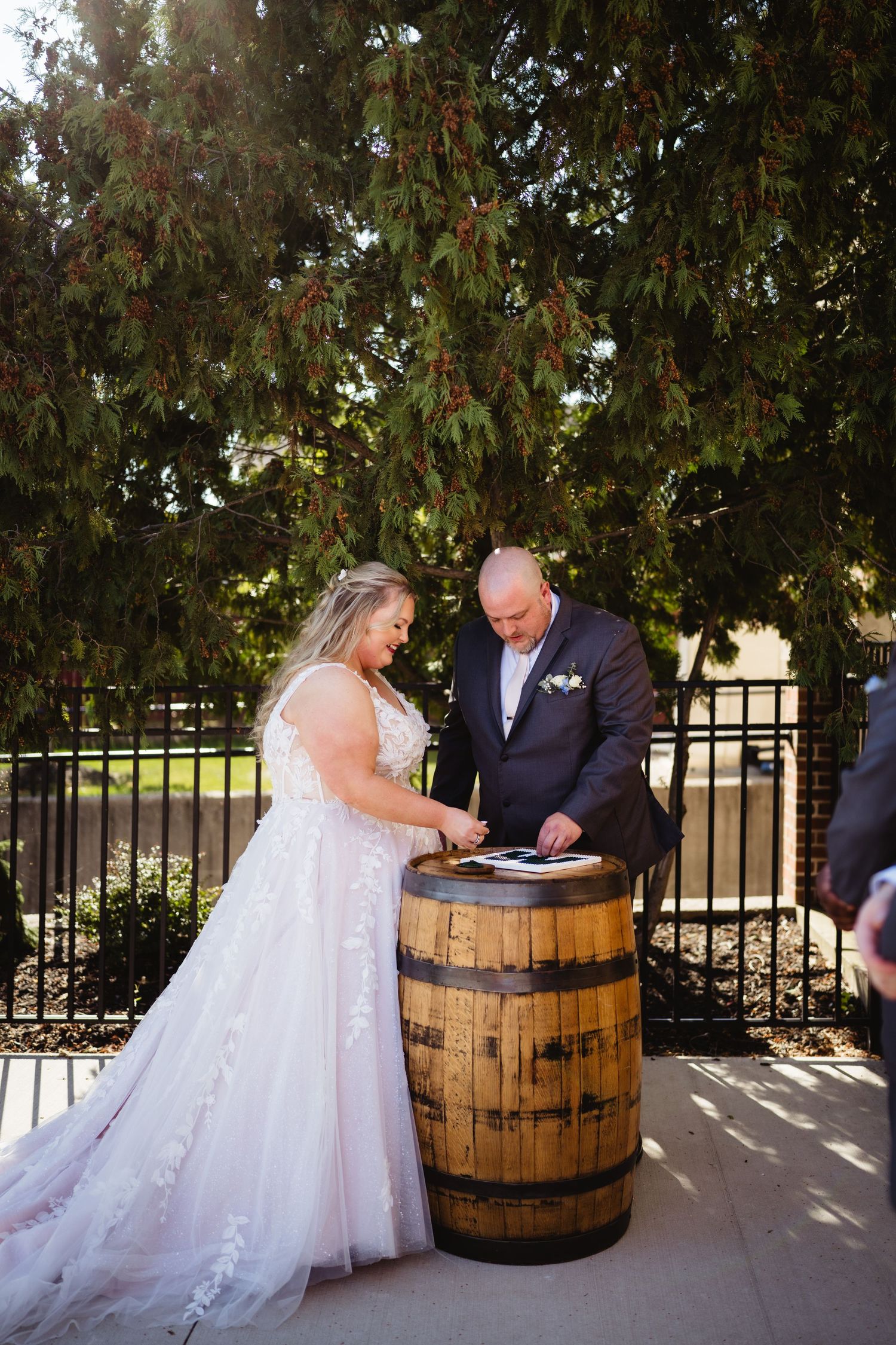 A couple signs documents on a rustic wooden barrel during an outdoor wedding ceremony.