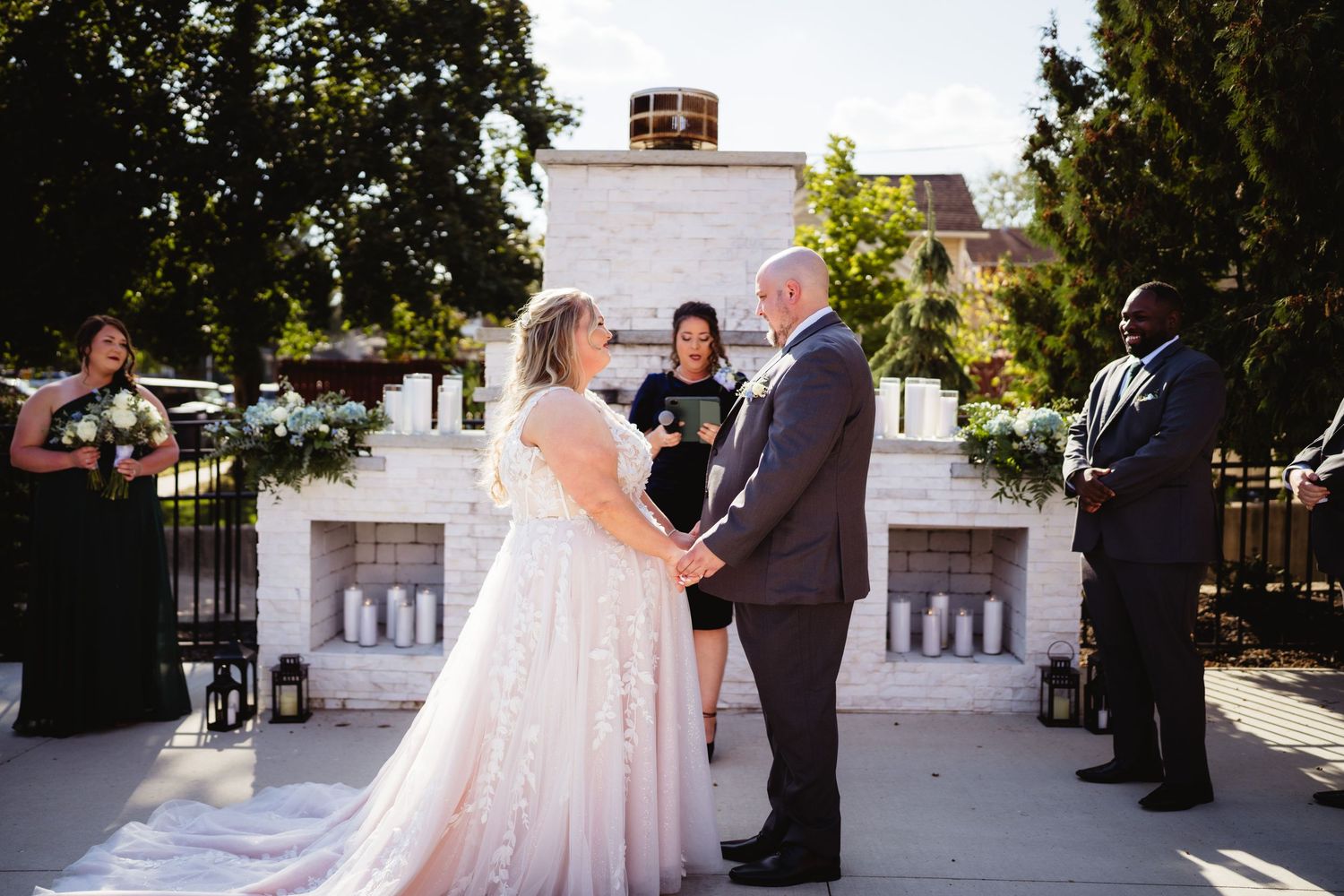 Outdoor wedding ceremony scene with guests gathered in front of a white building on a sunny day.