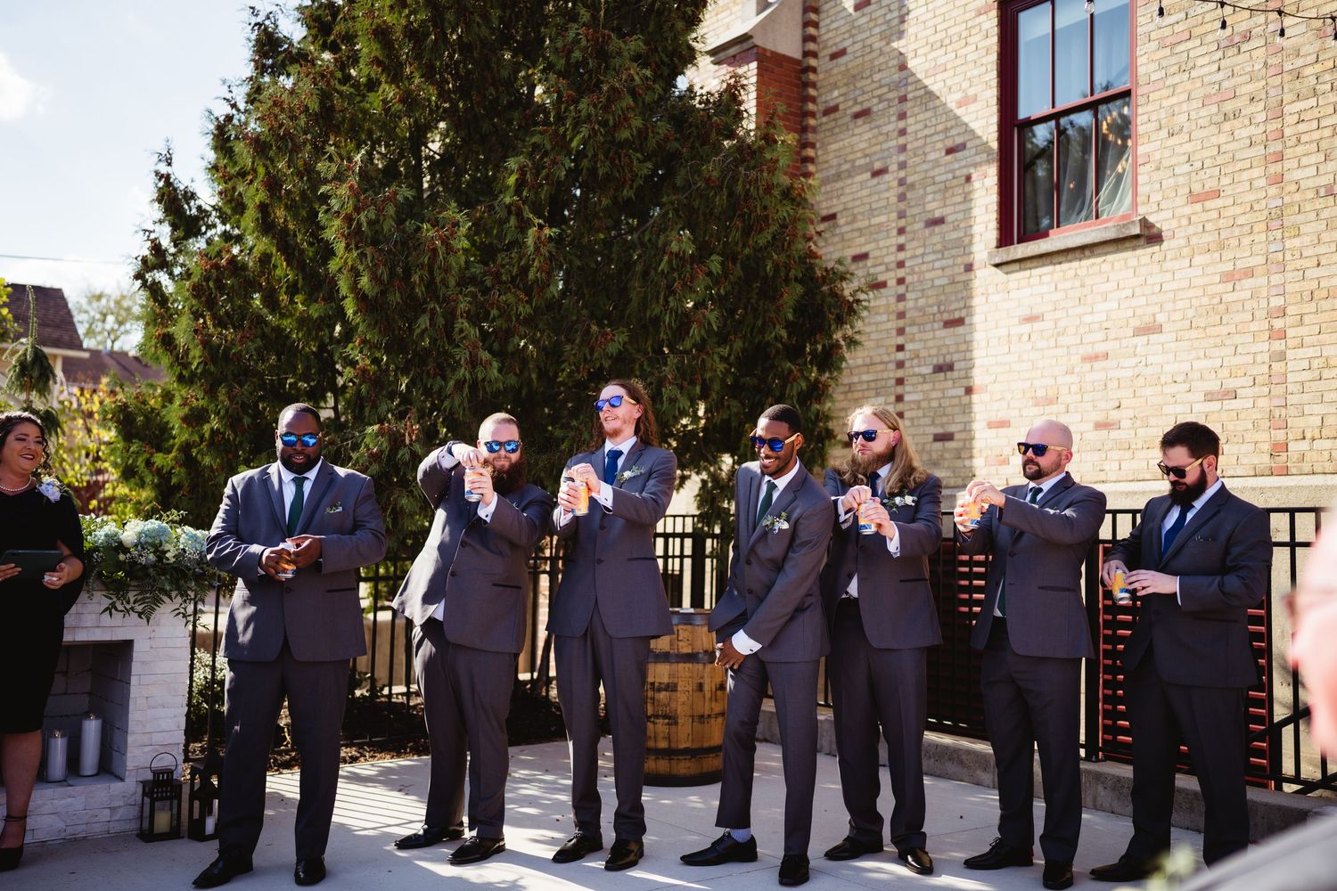 Wedding party members stand in a row outside a brick building during a formal celebration ceremony.