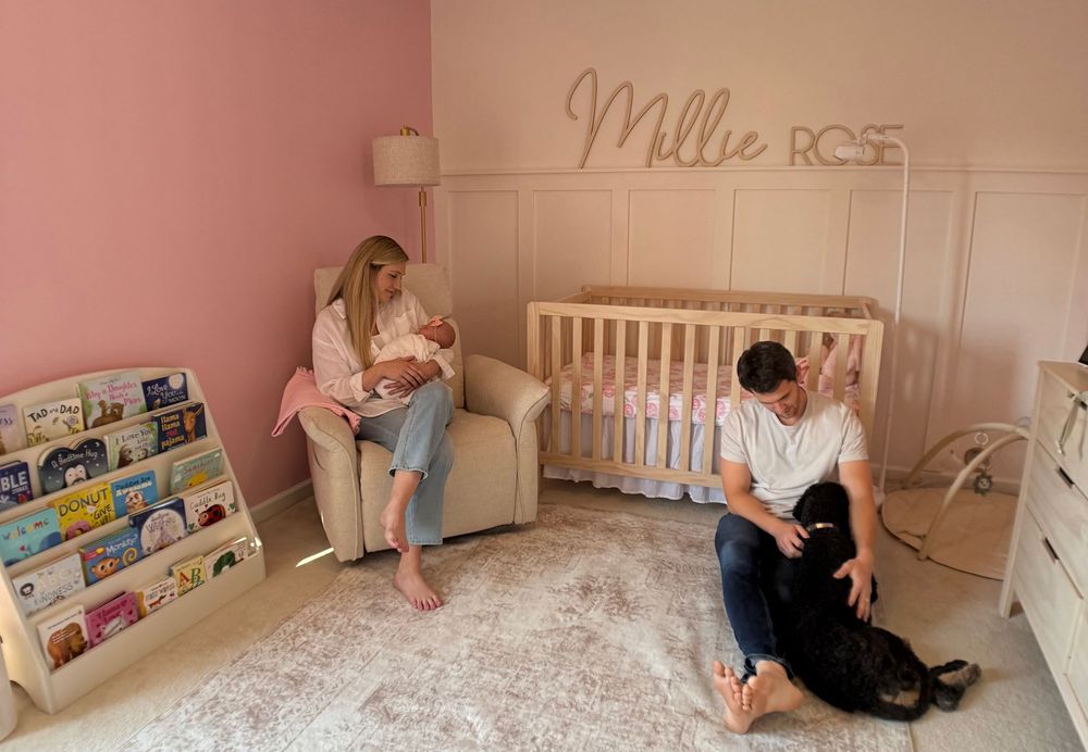 Parents with newborn in pink nursery room with Millie Rose name sign and dog.