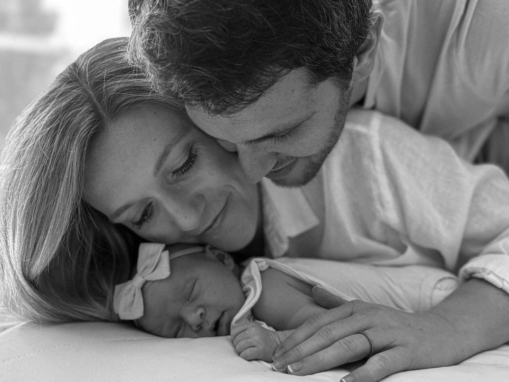 Black and white photo of parents lovingly looking at their sleeping newborn baby.