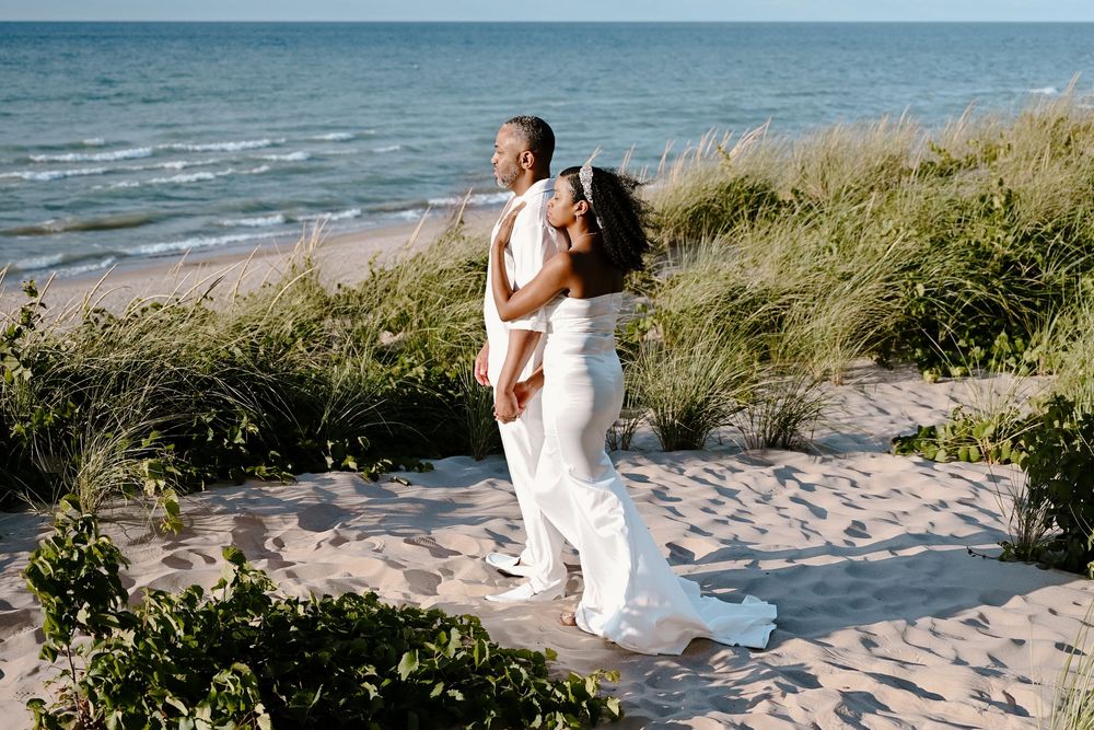 A person in white attire practices yoga poses on a sandy beach with ocean waves and dunes in the background.