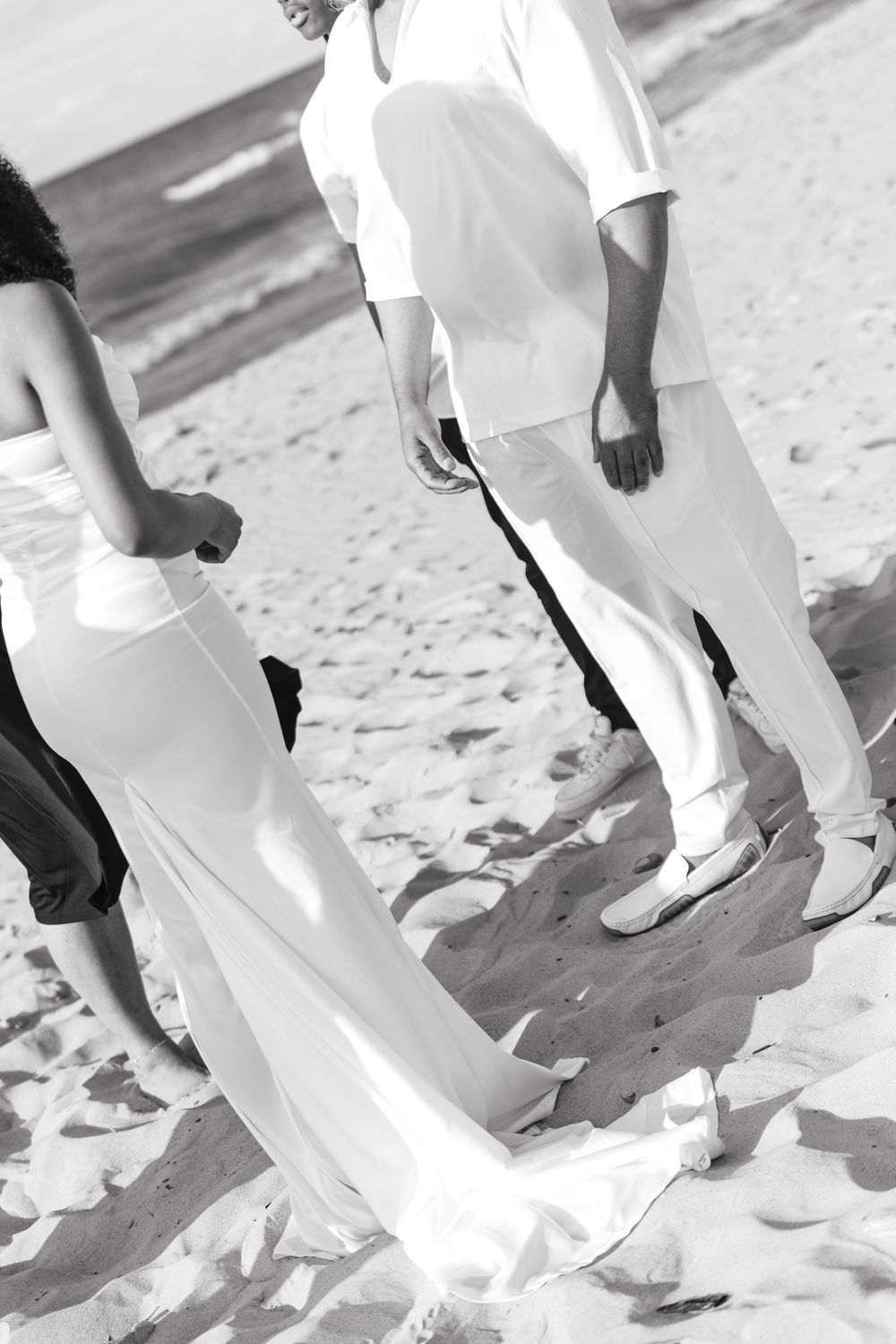 Multiple people wearing white clothing walk on a sandy beach in black and white photography.