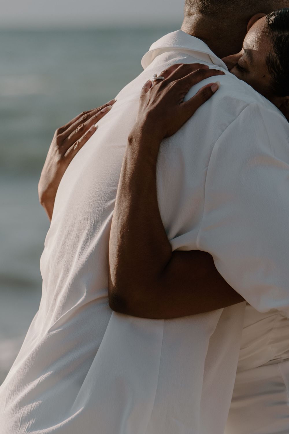 A series of intimate embraces between two people wearing white clothing against an ocean backdrop.