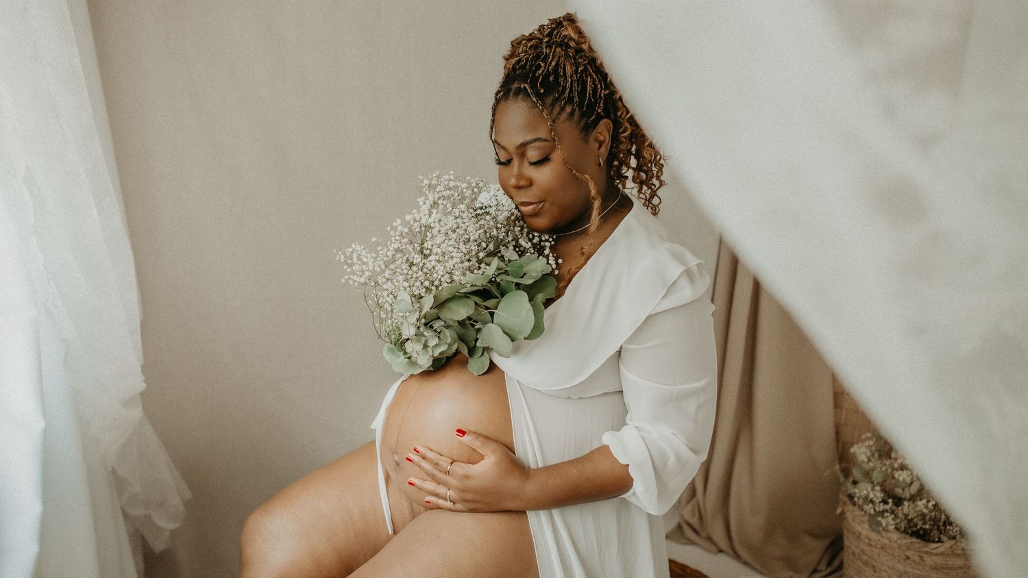 A series of maternity photos showing a pregnant woman in a white dress holding baby's breath flowers against a neutral backdrop.