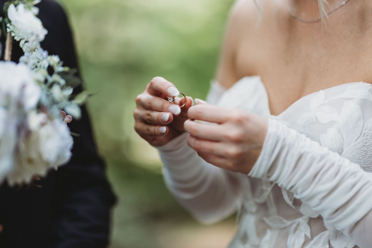 Wedding party members hold white floral bouquets while checking their phones during an outdoor ceremony.