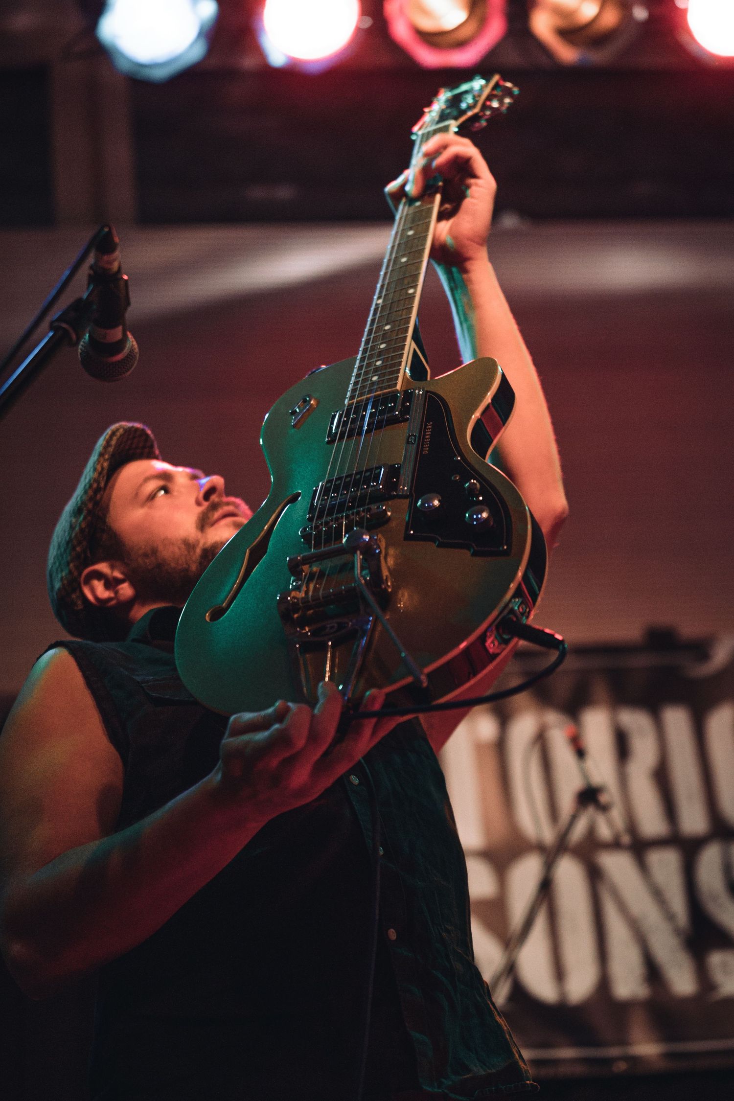 Guitarist performs on stage with a green electric guitar under dramatic concert lighting.