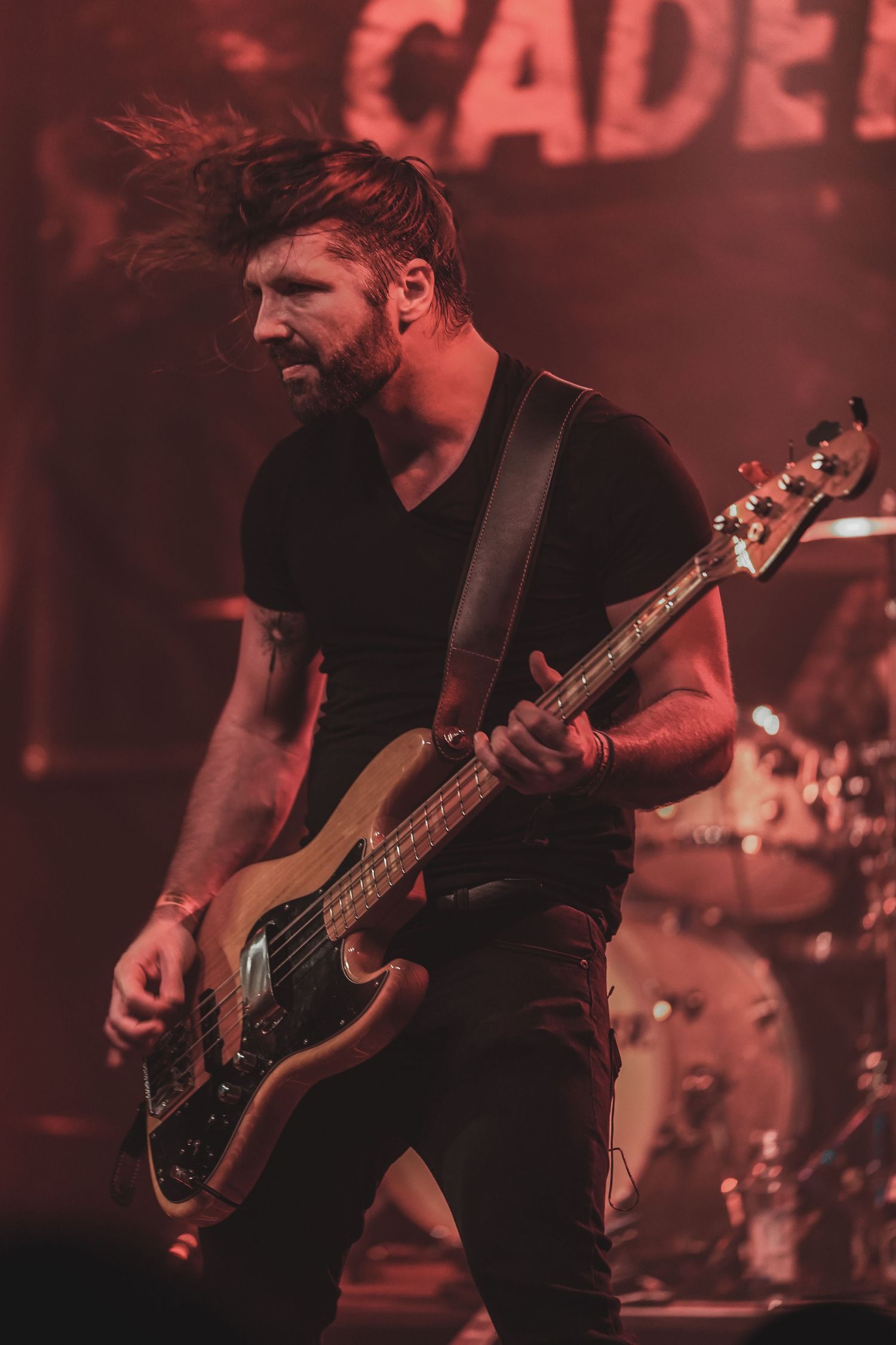 Bass guitarist performs on stage in dark red lighting during a rock concert performance.