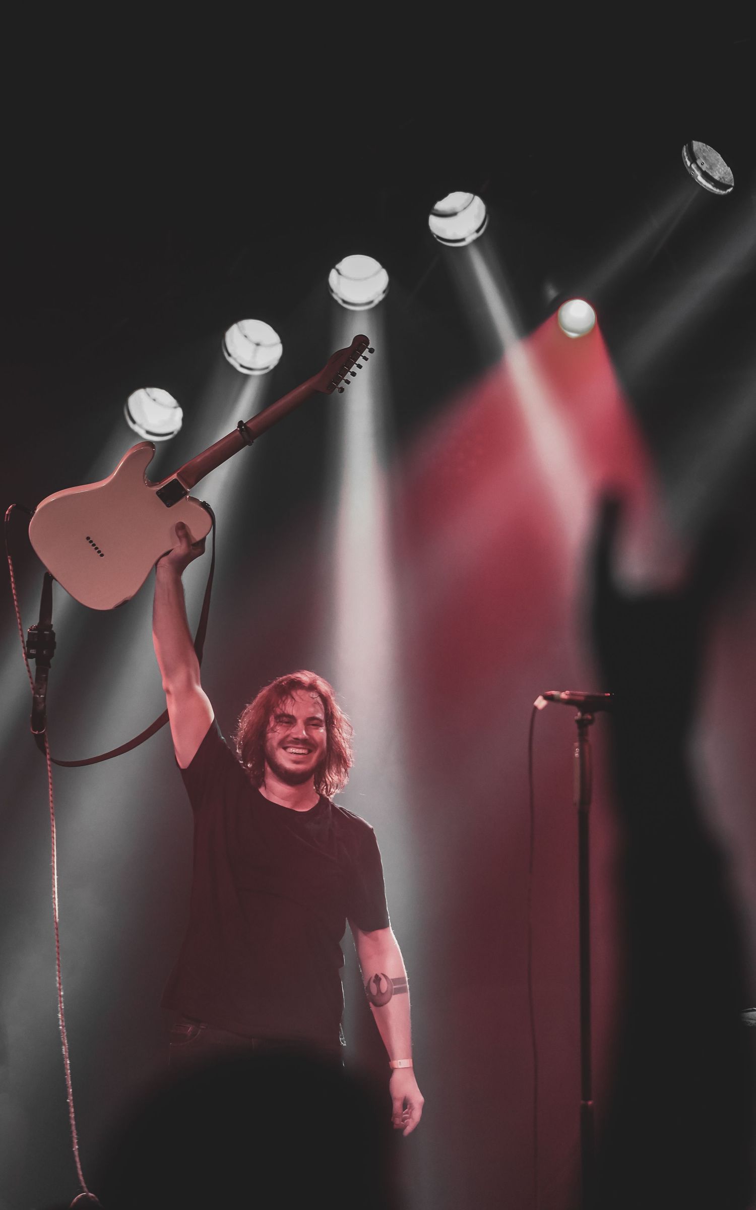 Performer silhouetted against dramatic white spotlights on a dark concert stage.