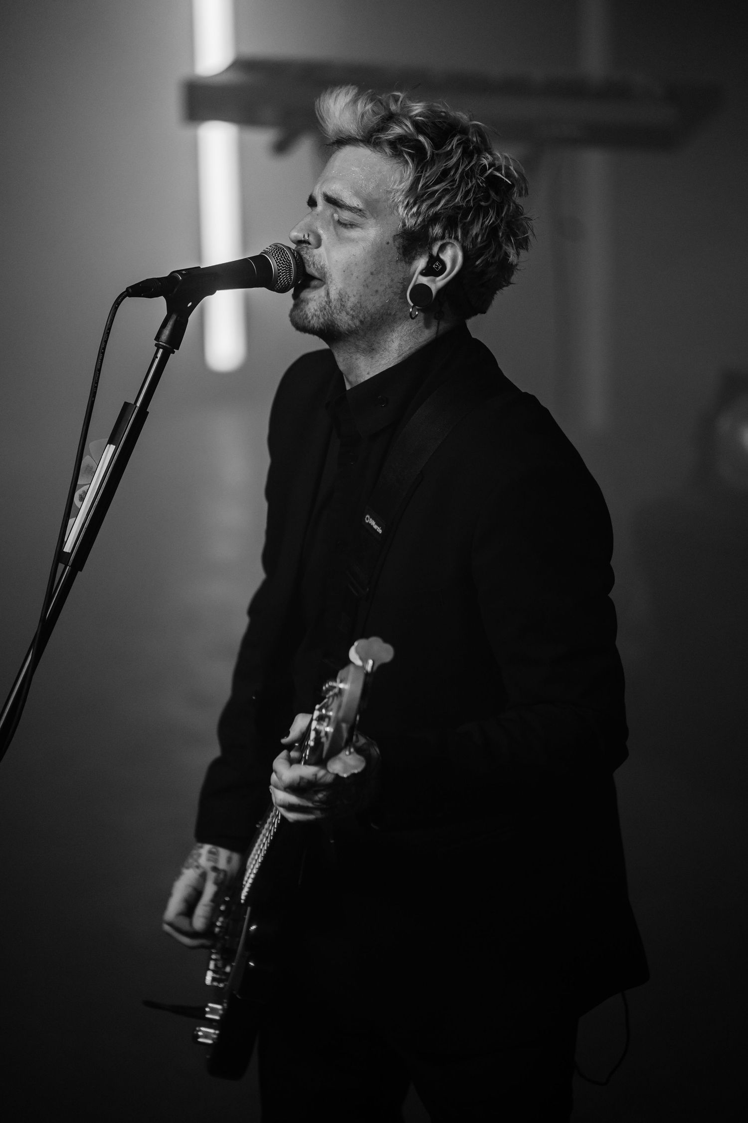 Black and white photo series of a musician performing on stage with a microphone in dark lighting.