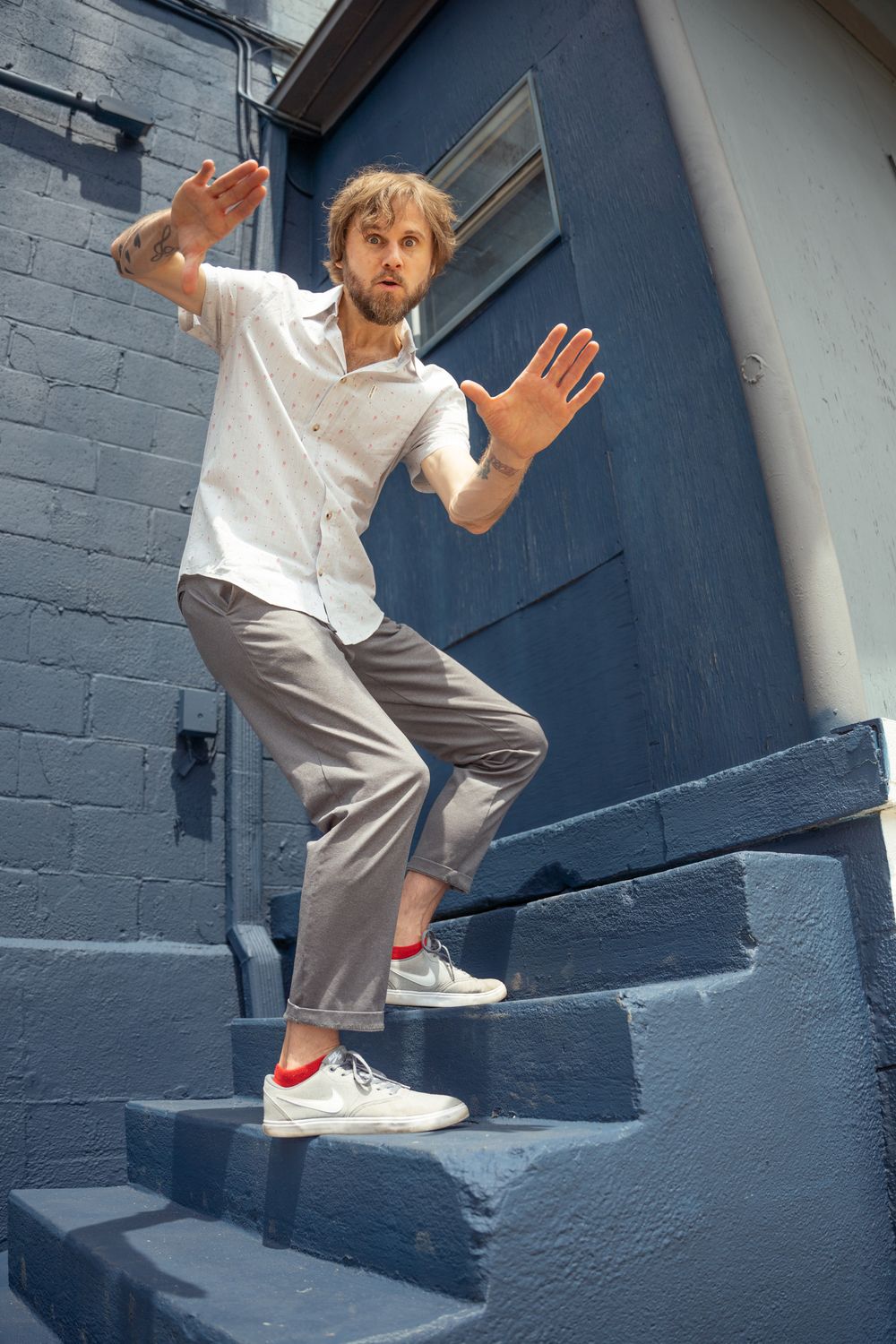 Action portrait of a man in a white tee and grey trousers running up a blue industrial staircase; dynamic commercial lifestyle photography i