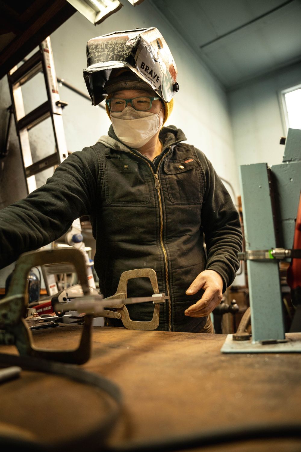 An artisan wearing a welding mask working in a technical studio; commercial brand photography for local Italian makers and designers.