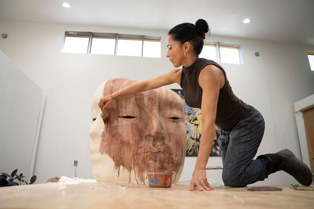 An artist in a black top working on a large clay sculpture in a bright Florence studio; creative editorial portrait emphasizing form and tex