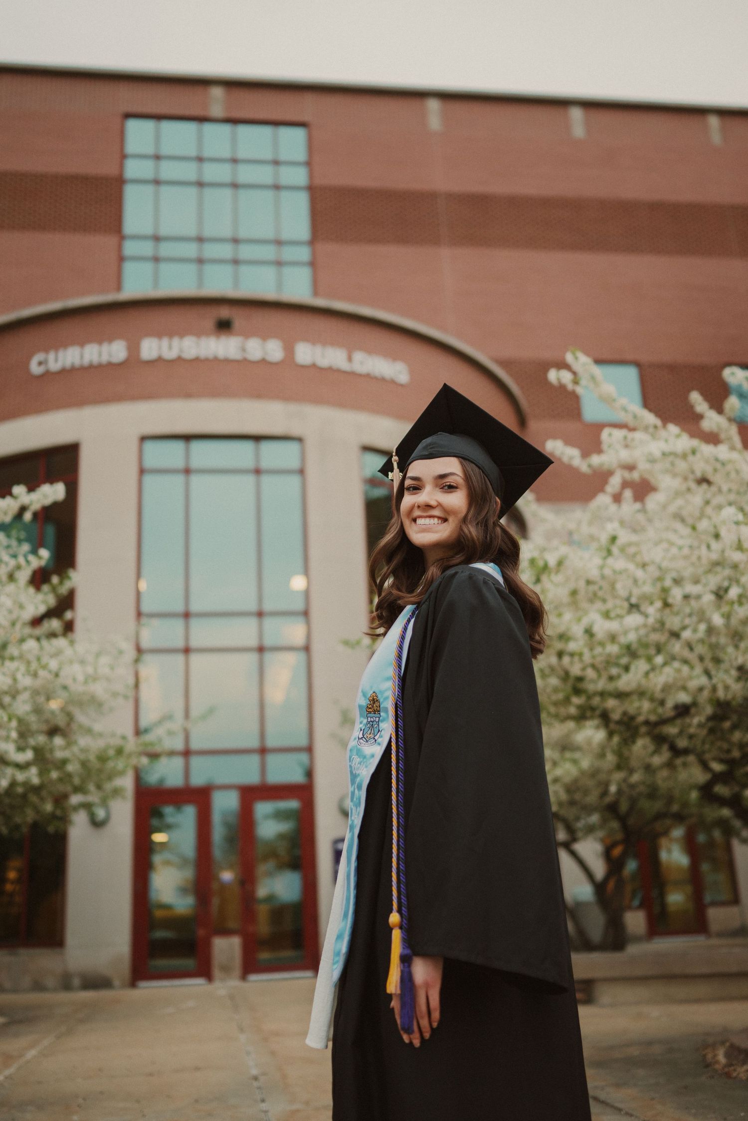 Graduation photoshoot in front of a business building with blooming trees.