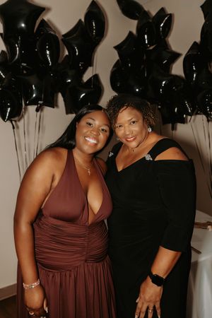 Two people embrace and smile at a celebration decorated with black balloons and elegant decor.