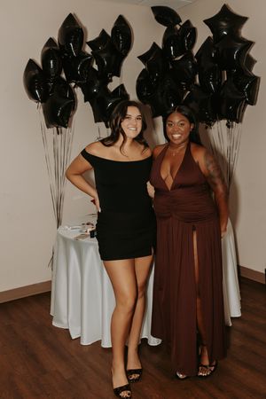 Friends pose together at a party with black balloons in the background.