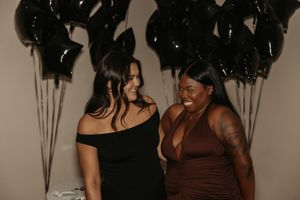 Two friends in contrasting brown and black dresses pose together at a celebration with star decorations.