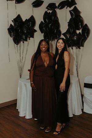 Two friends pose together at an event with black star balloons and white decor in the background.