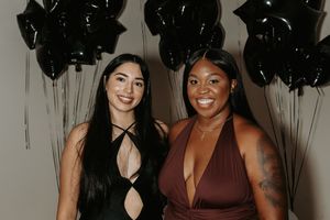 Two friends in evening attire pose together against a backdrop of black star-shaped balloons.
