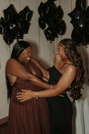 Two people share an emotional embrace at a celebration decorated with black balloons.
