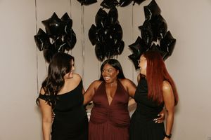 A group of friends in dark dresses posing together at a formal celebration event.