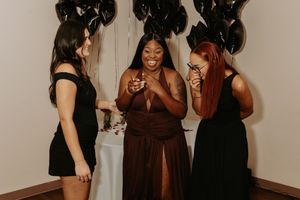 A group of people in formal attire laugh and smile together at a social gathering or party.