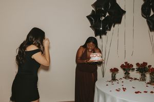 Festive party setup with black balloons, white tablecloth, and red rose petals scattered on floor.