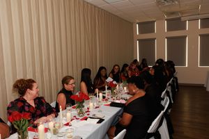 A formal event space with long tables decorated in white linens and red accents for a special occasion.