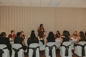 Long banquet table setup with white chair covers and formal place settings at an indoor event.