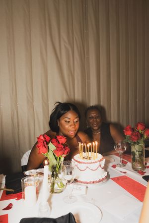 A birthday celebration setup with lit candles on cake, red roses, and wine glasses on white tablecloth.