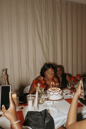 A dimly lit celebration with birthday candles glowing on a white frosted cake at an elegant table setting.