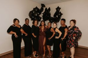 A group of party guests posing together in black attire against a light colored wall.