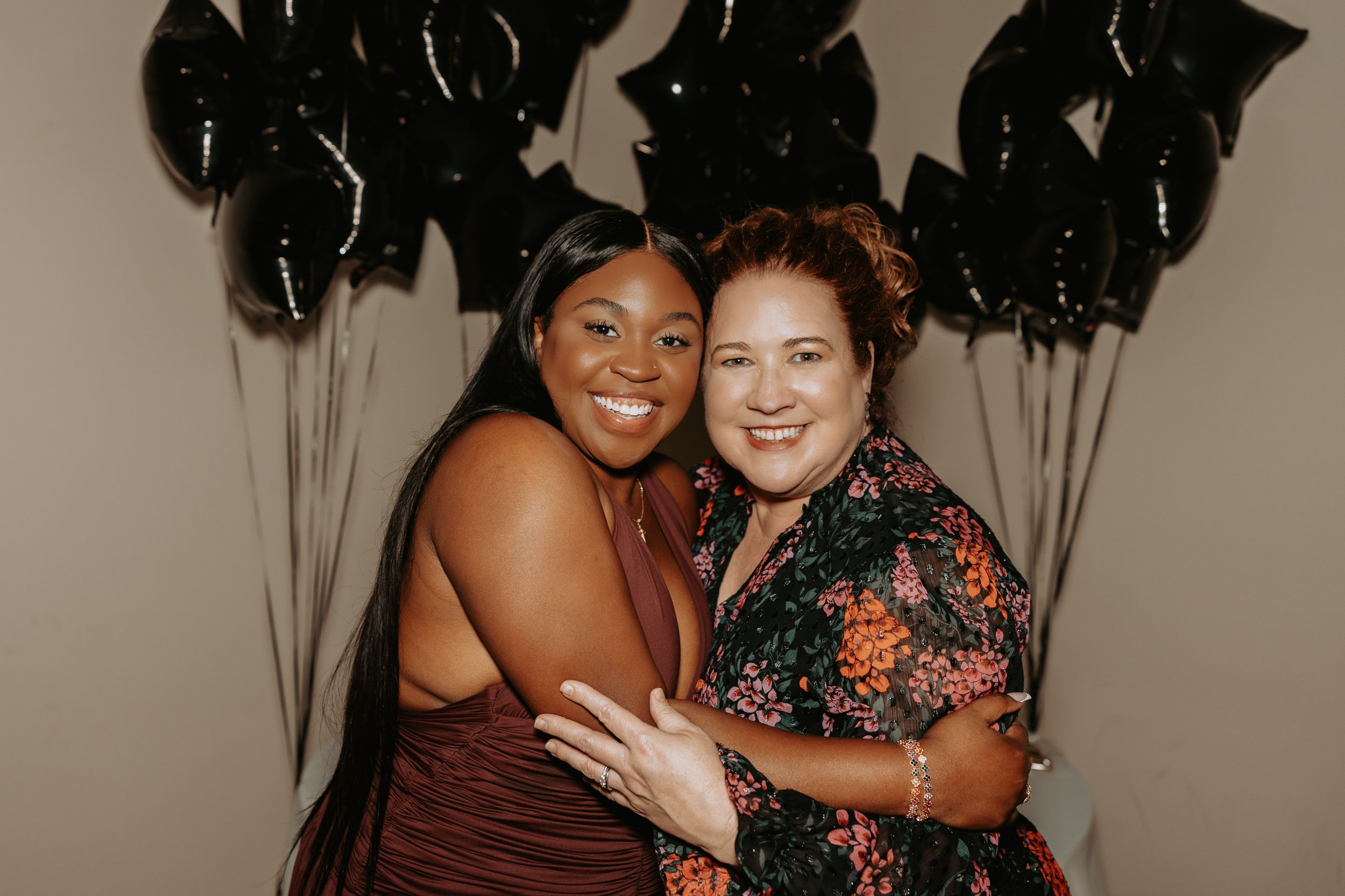 Two people smiling and embracing while posing for photos at what appears to be a social gathering or celebration.