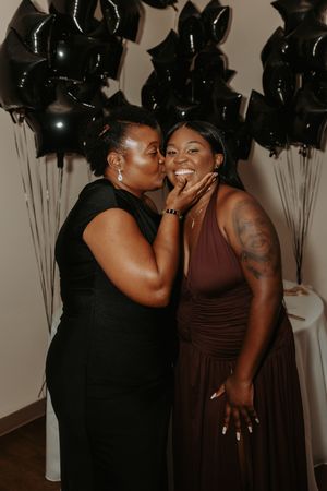 Two people sharing an intimate moment while laughing together against a backdrop of black balloons.