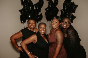 A group of friends pose together in black and brown outfits against a dark background for a stylish photo shoot.