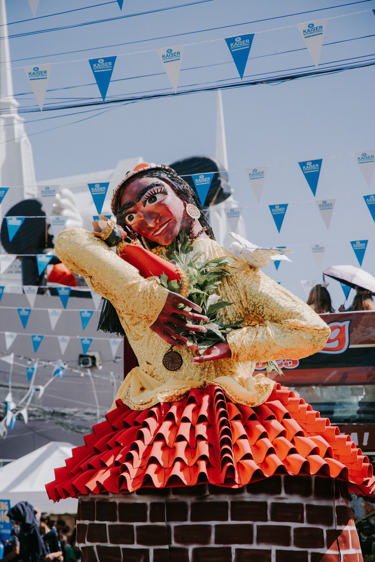 Ornate golden decorative pieces displayed on red pleated platforms under blue festival banners.