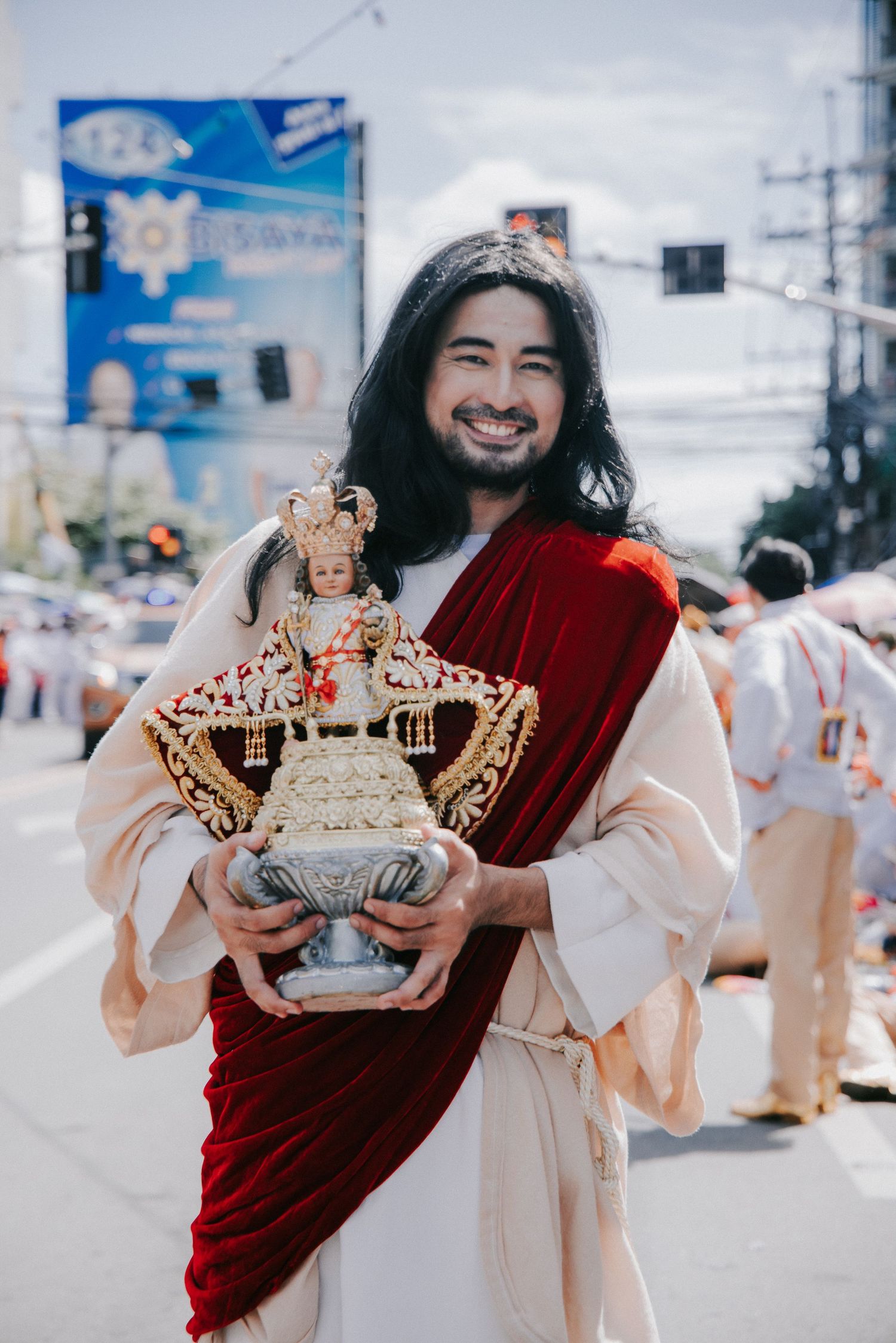 Person in red and white robes holds ornate golden crown during cultural festival.
