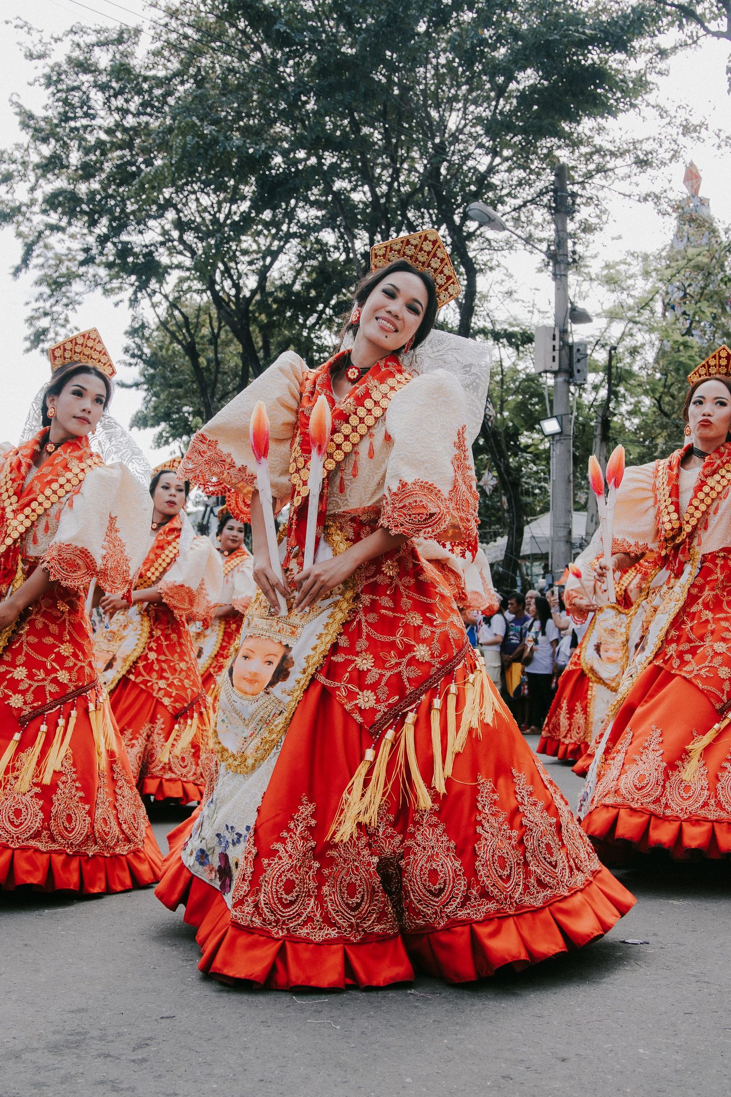 Dancers in vibrant red traditional gowns perform synchronized movements at street festival.