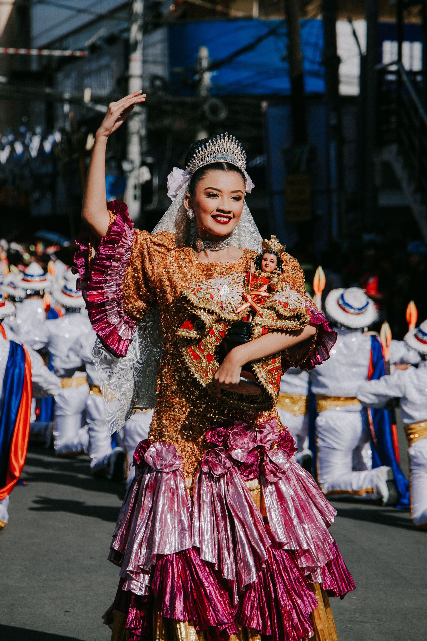 Performers in sparkly pink and gold costumes dance during street festival celebration.