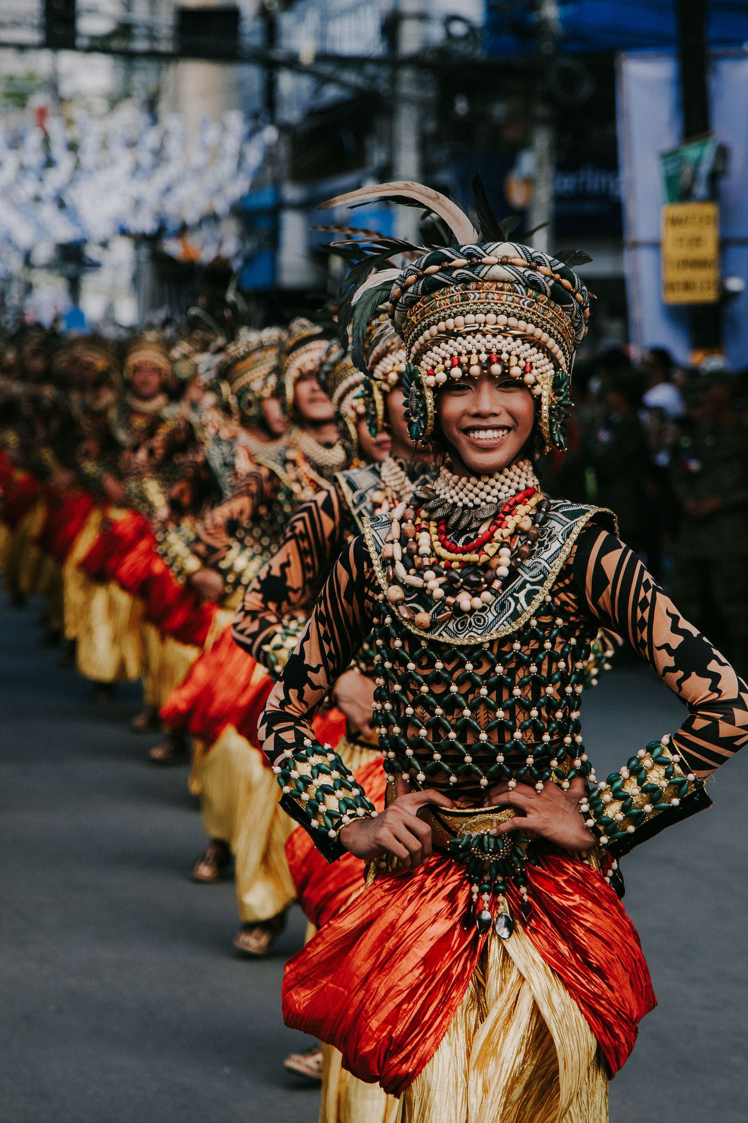 Dancers in traditional black and red costumes with ornate headdresses perform in street parade.
