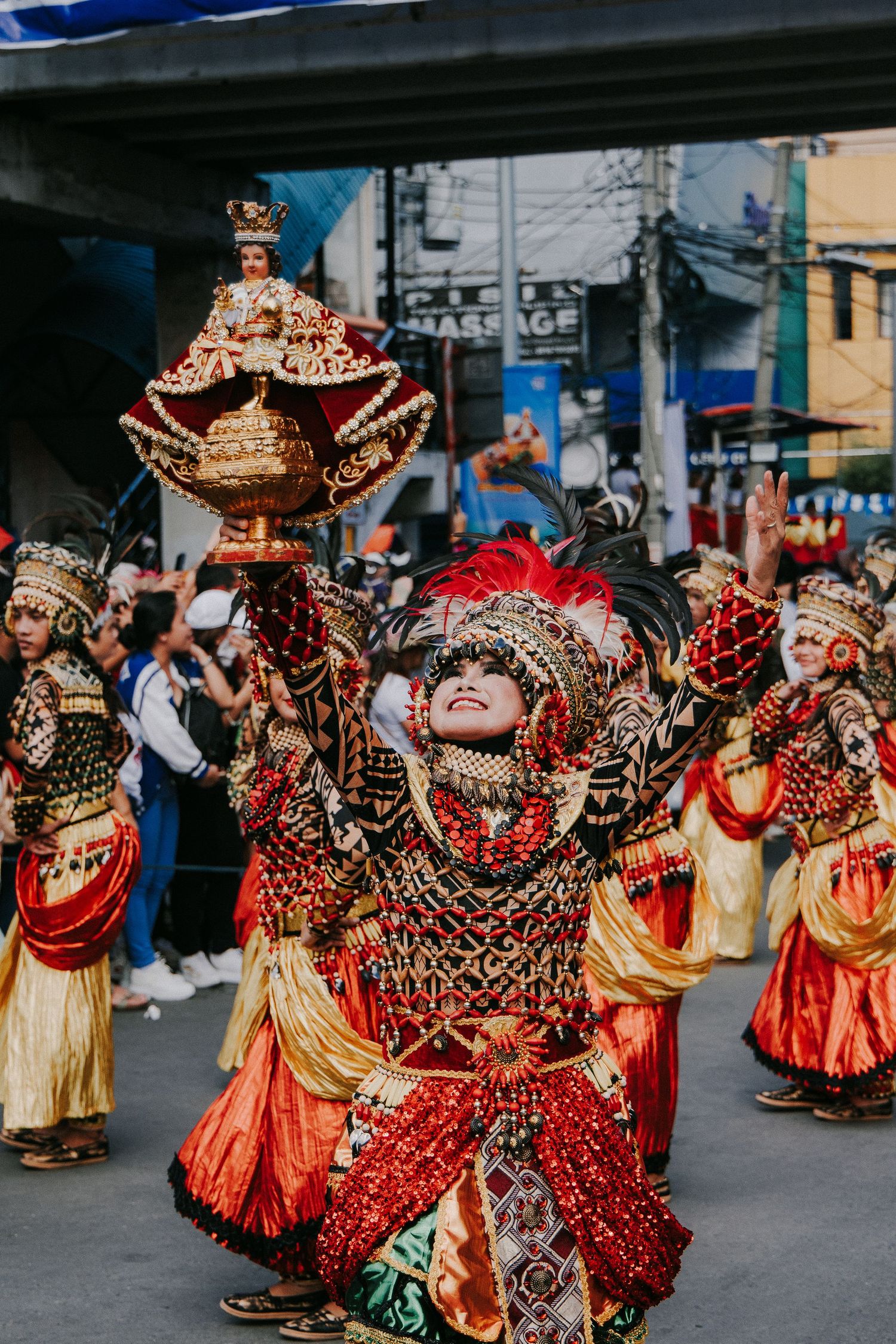 Performers in vibrant red and gold traditional costumes dance during a cultural festival parade.