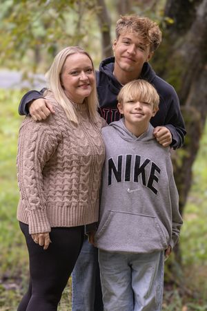 A family wearing casual sweaters and hoodies poses together outdoors against an autumn backdrop.