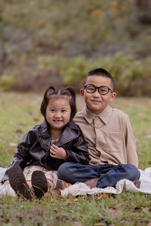 Two children sitting together on a blanket outdoors wearing coordinated outfits in autumn.