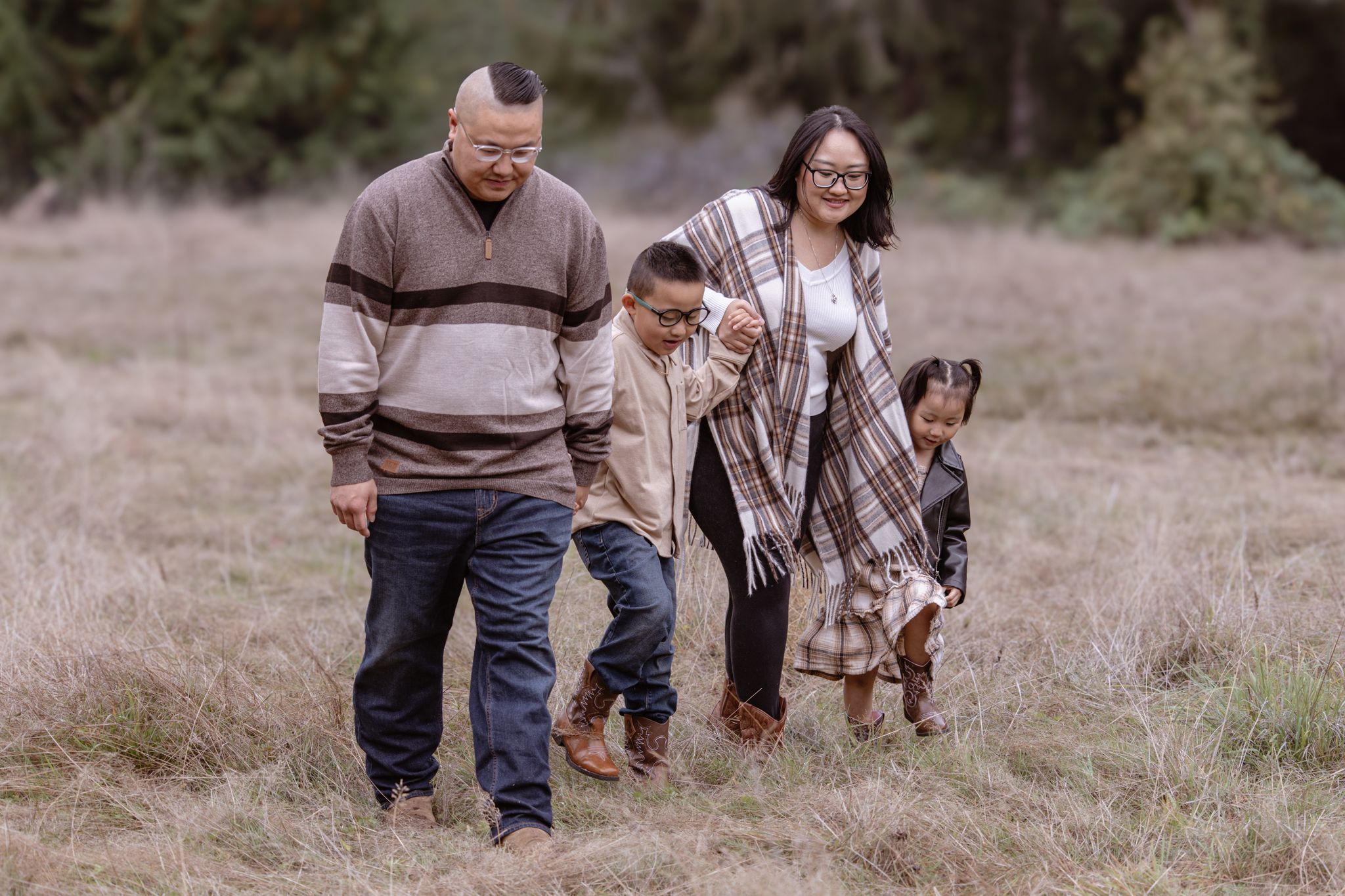 A family walks together through a grassy field on an autumn day wearing coordinated brown and white sweaters.