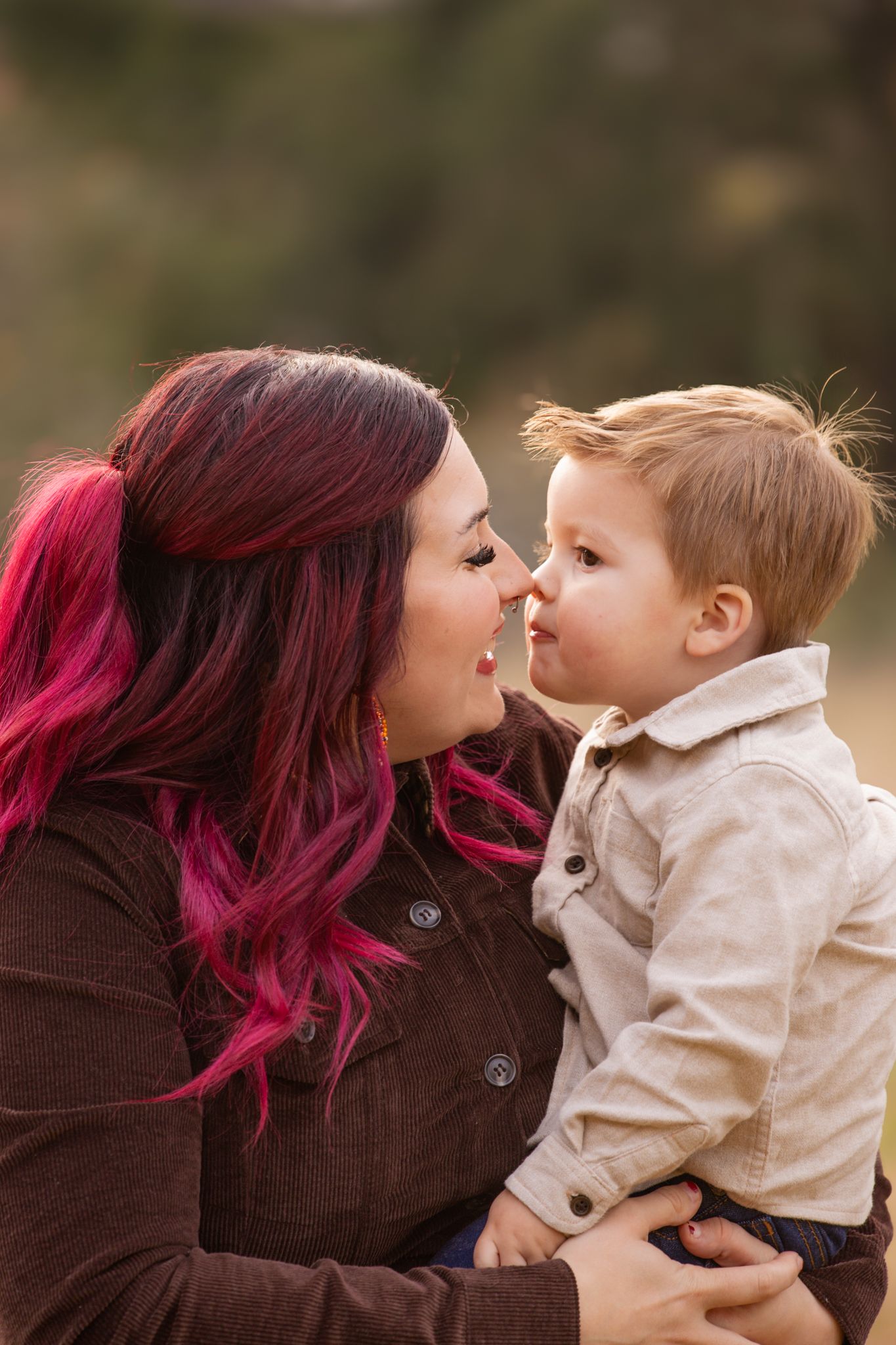 A tender moment shared between parent and toddler with vibrant pink hair against a soft blurred background.