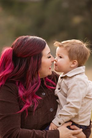 A tender moment shared between parent and toddler with vibrant pink hair against a soft blurred background.