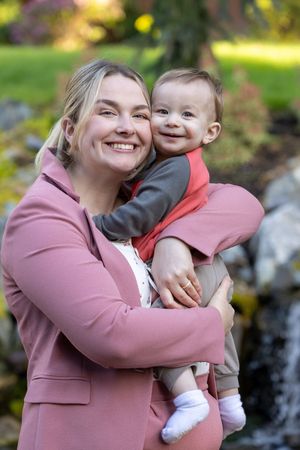 A heartwarming outdoor portrait of parent and baby smiling together in front of a garden with a pink jacket.