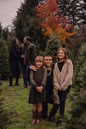 Family poses together among evergreen trees and autumn foliage during outdoor fall photo session.